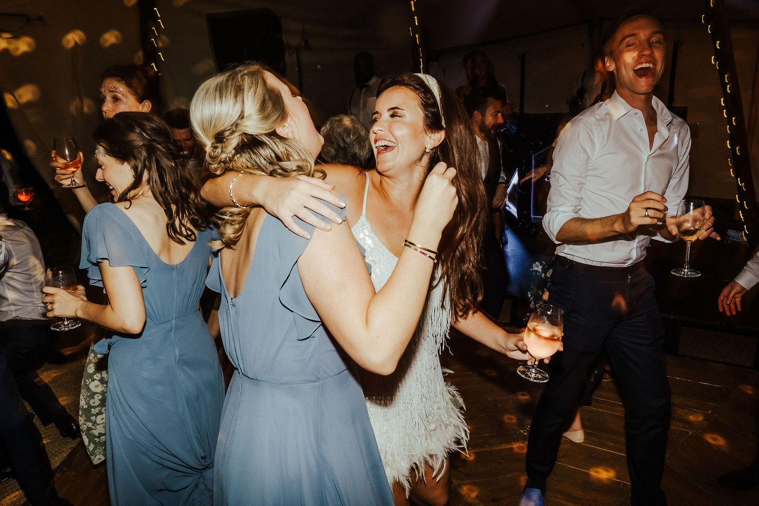 Wedding guests in blue dresses dancing and embracing on the dance floor.