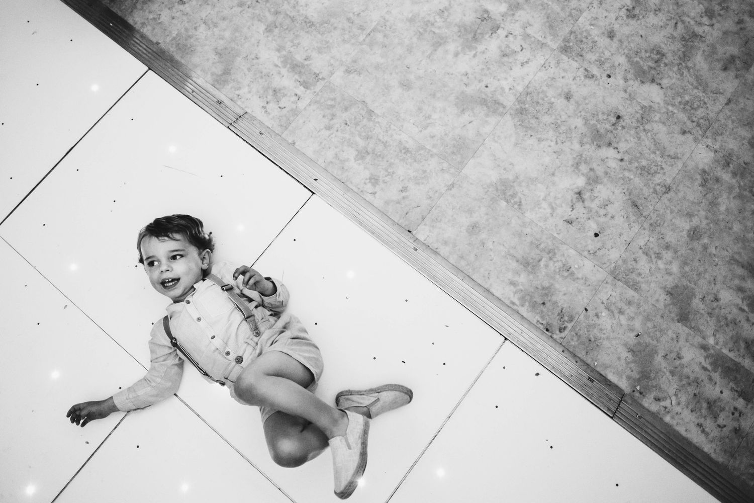 A playful black and white photo of a small child lying on a white floor.
