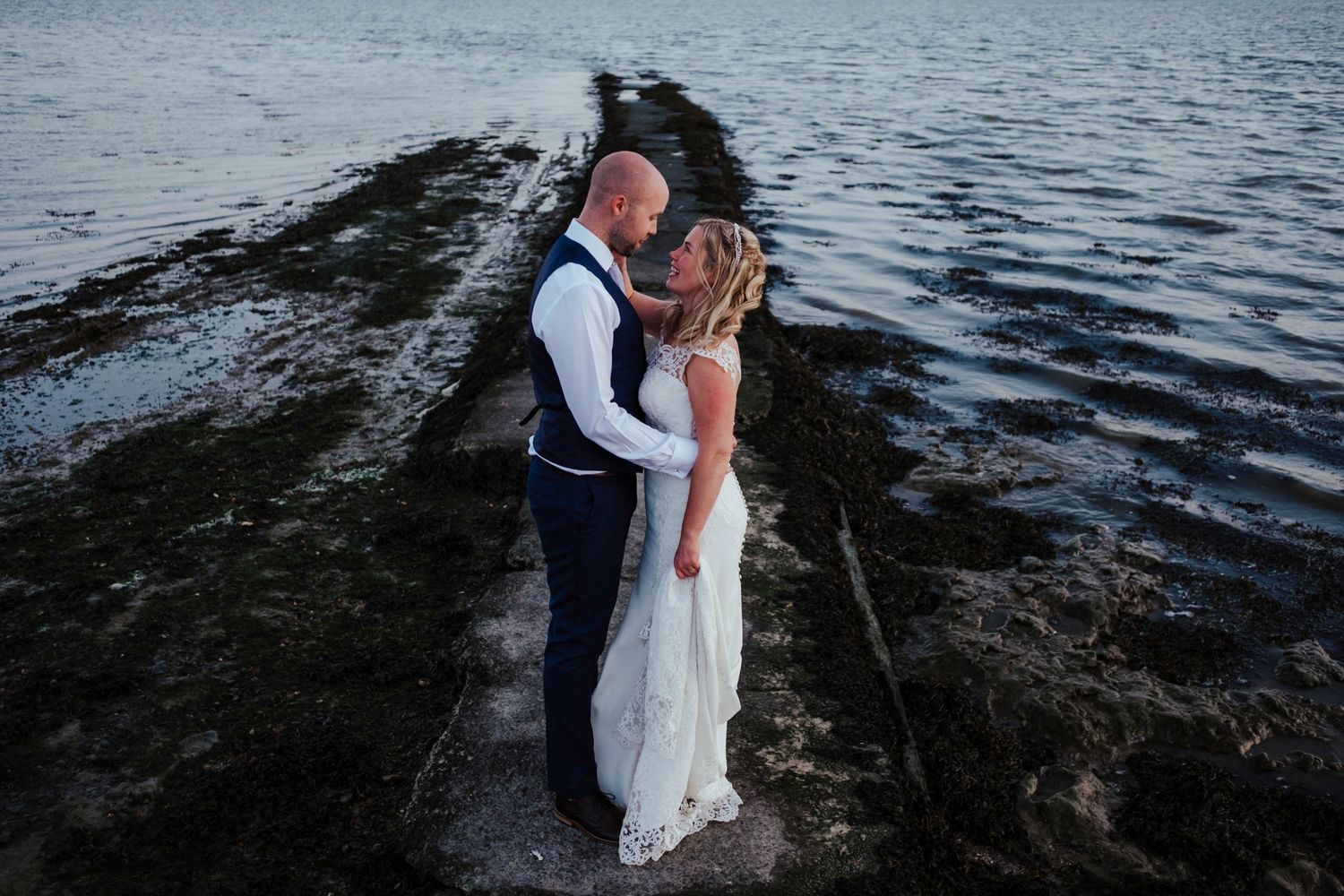 A couple shares an intimate moment on a rocky beach during their wedding photoshoot.