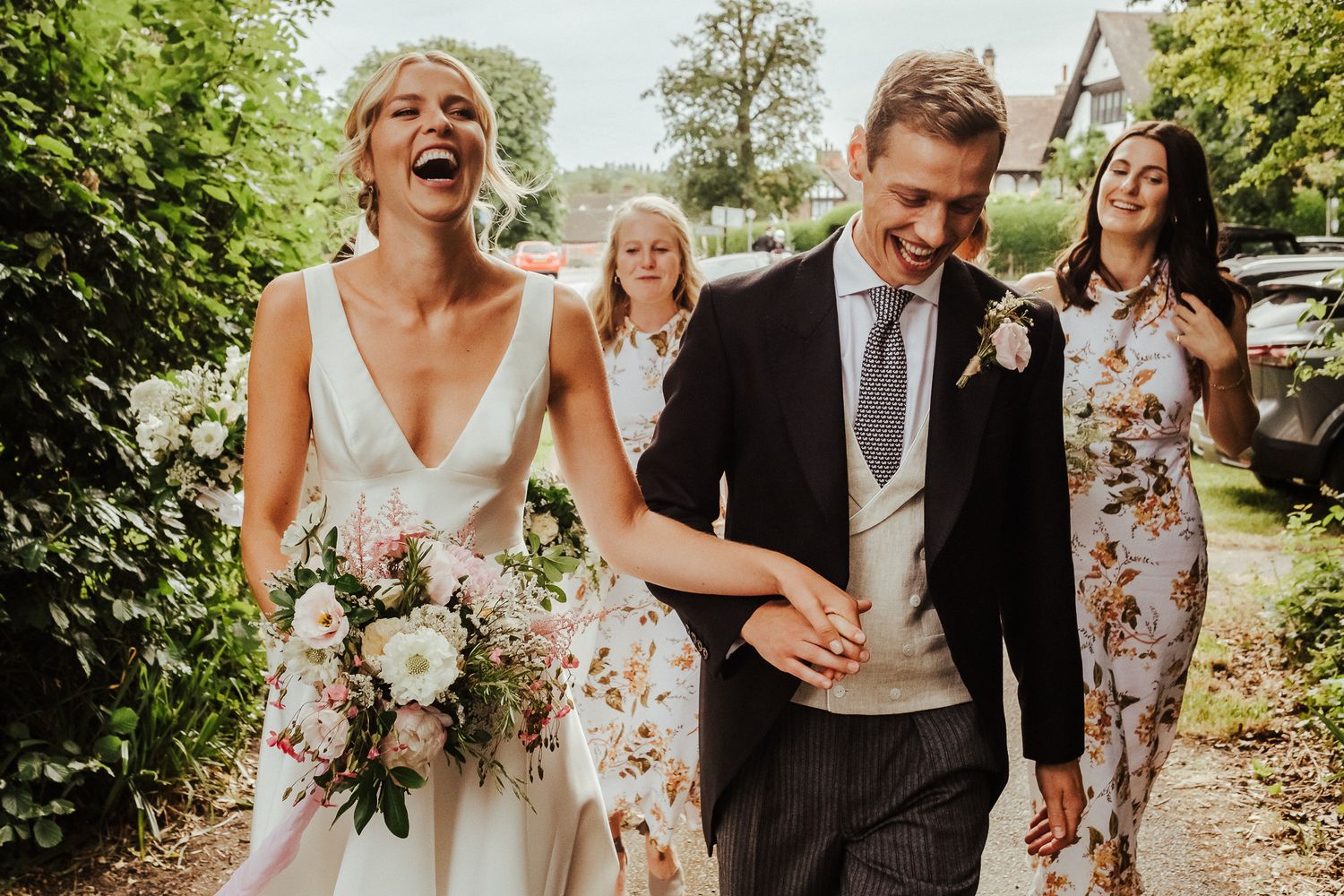 Joyful newlyweds share a laugh while walking through gardens with wedding party.