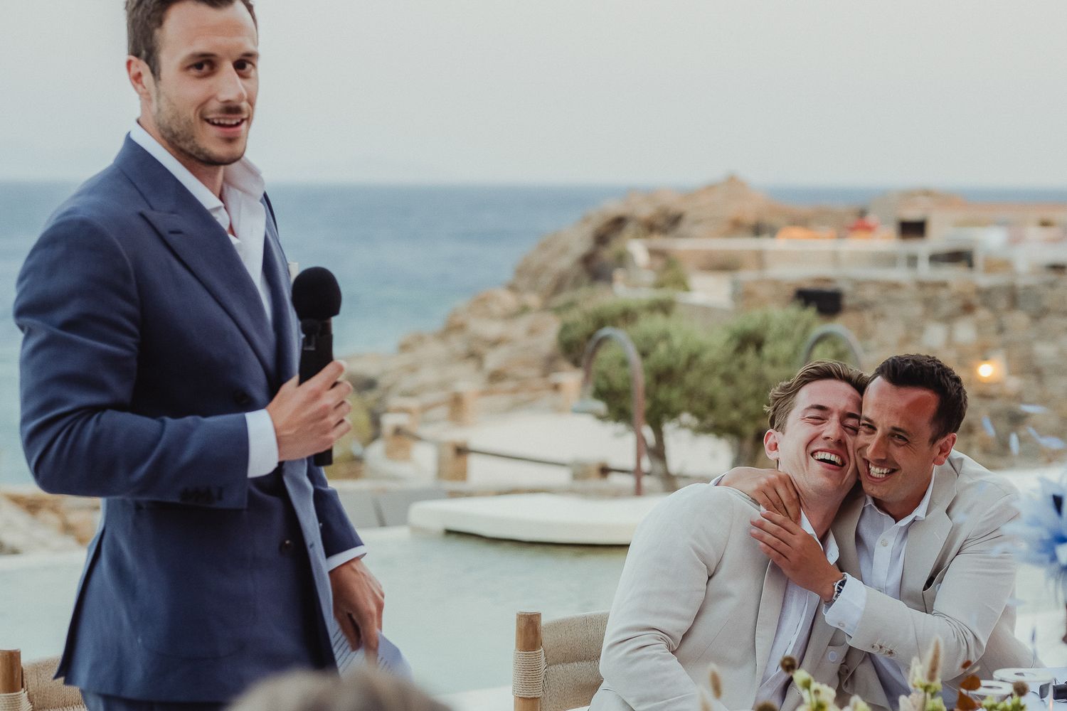 Wedding guests laughing and smiling during an outdoor celebration by the ocean on a sunny day.