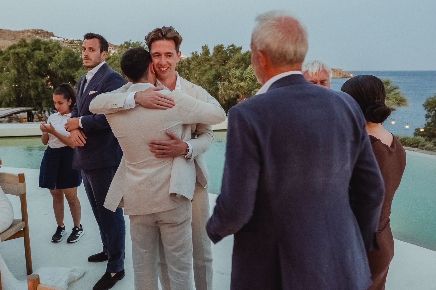 A series of emotional embraces between people at an outdoor seaside wedding ceremony.