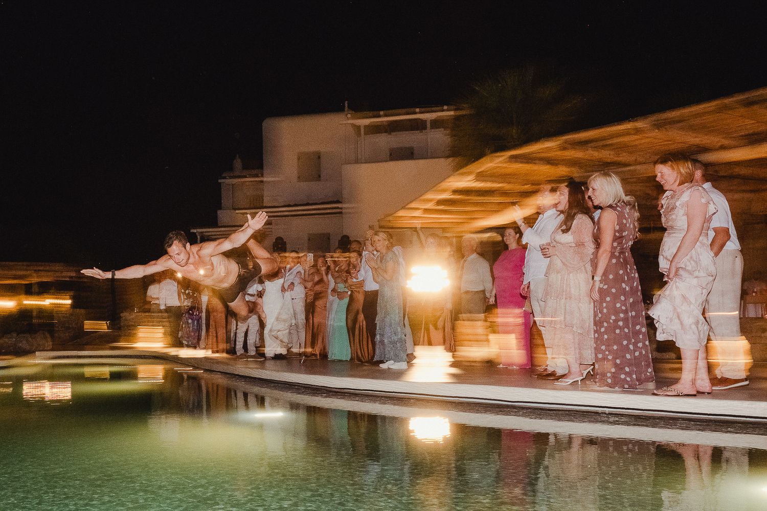 A nighttime wedding ceremony illuminated by warm lights beside a reflective pool creating a romantic ambiance.