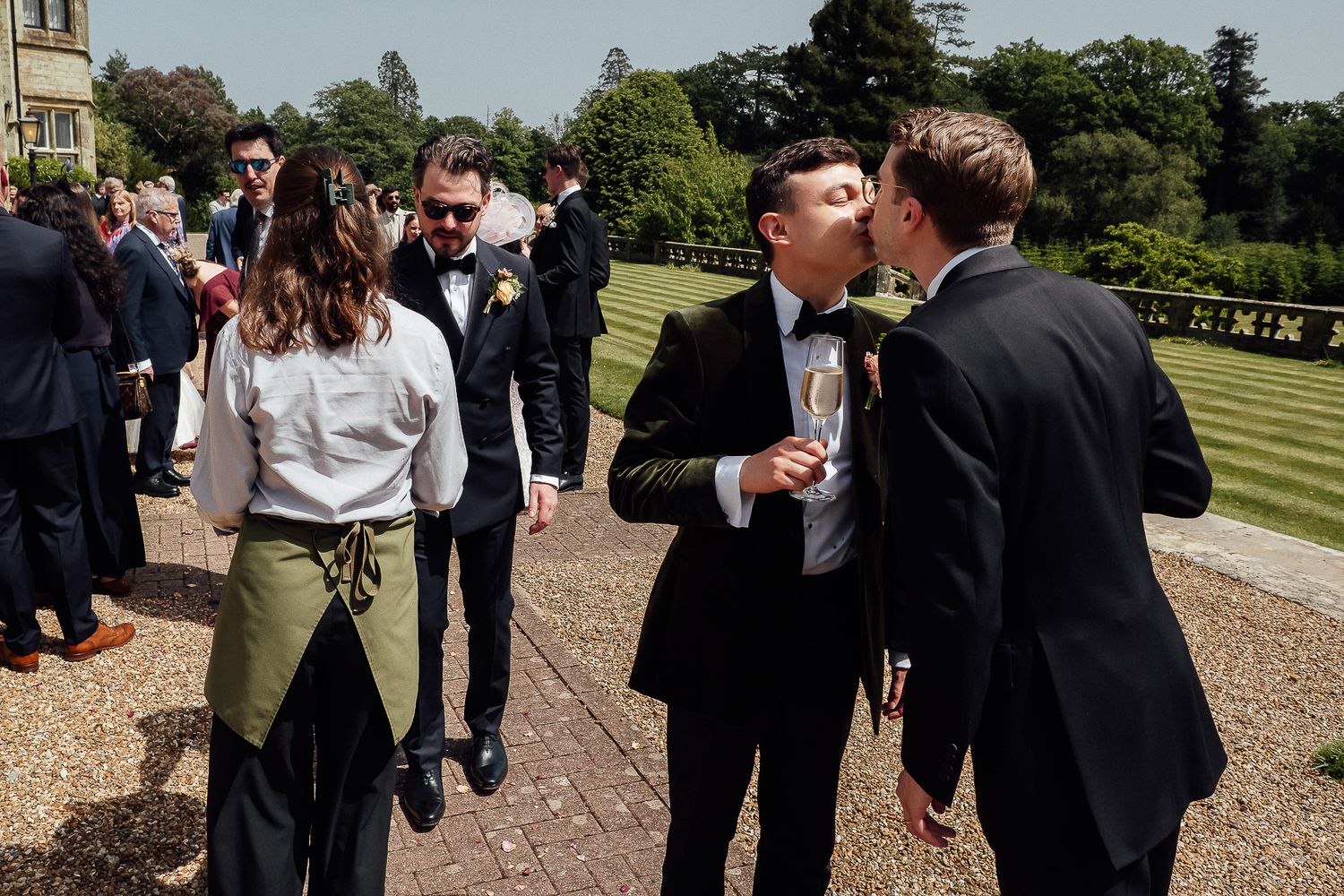 Guests in formal attire socializing outdoors at a wedding reception on a sunny day.