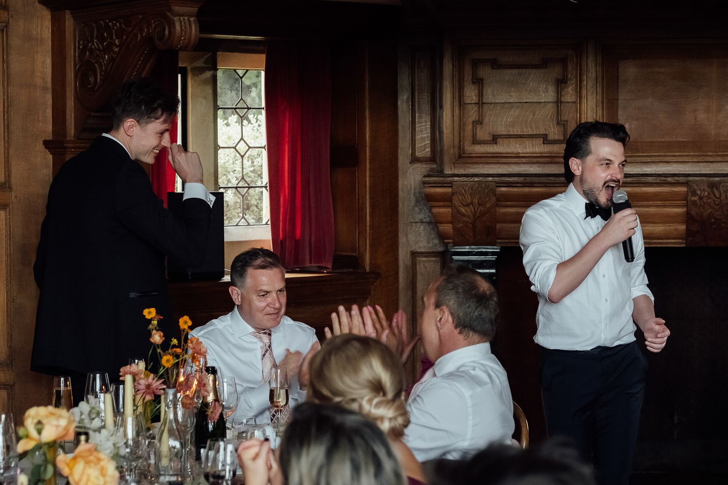 Man giving a speech with a microphone at an elegant wedding reception dinner in a grand venue.