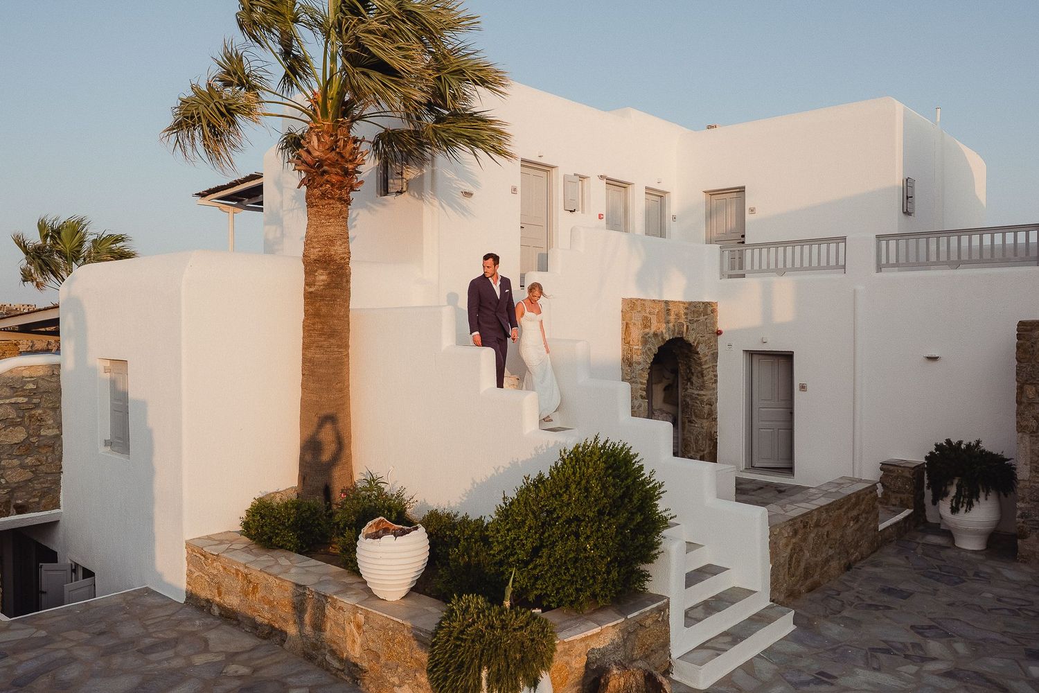 Mediterranean resort complex with white buildings, palm trees, and sunny walkways at sunset.