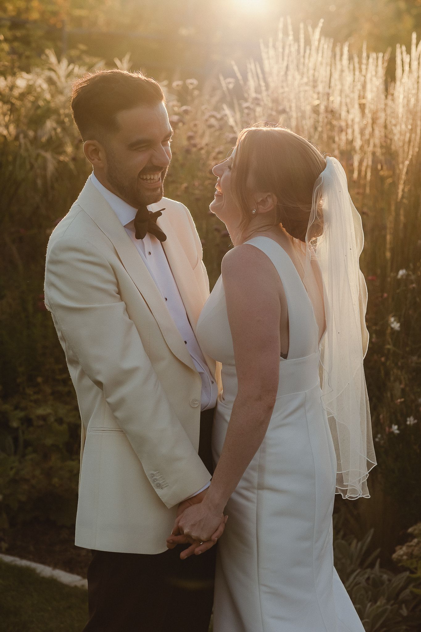 A couple shares an intimate moment in formal wedding attire during golden hour sunset in a natural outdoor setting.