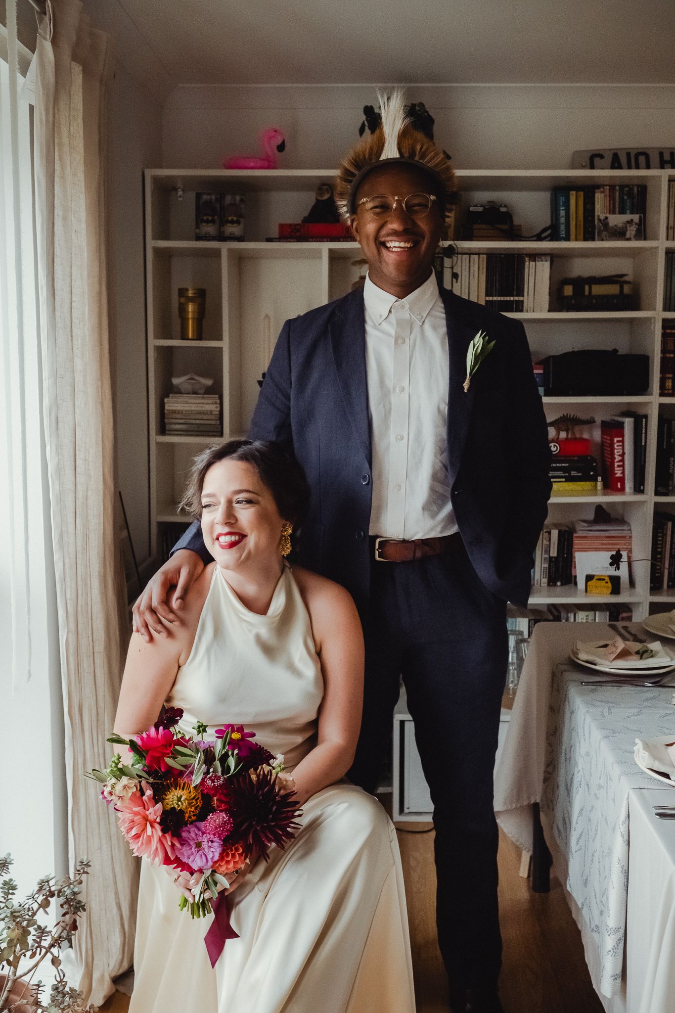 A joyful moment captured during a wedding celebration in a bright room with white bookshelves.
