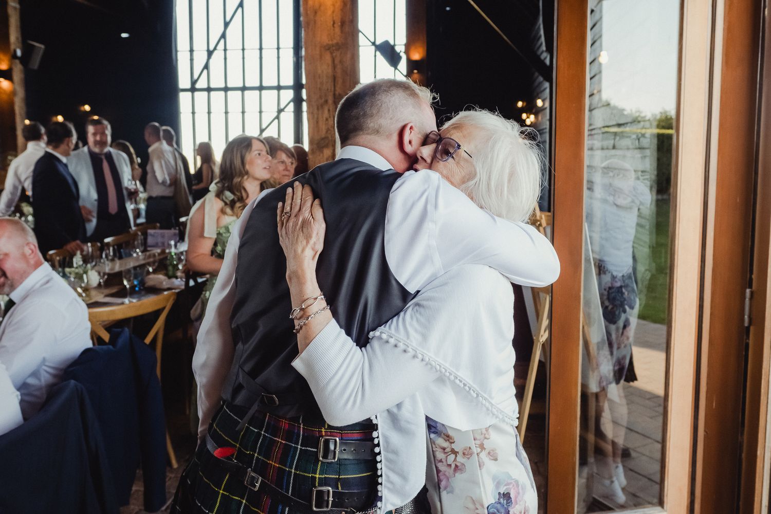 A tender embrace between newlyweds at a wedding reception, with the groom wearing a traditional Scottish kilt.