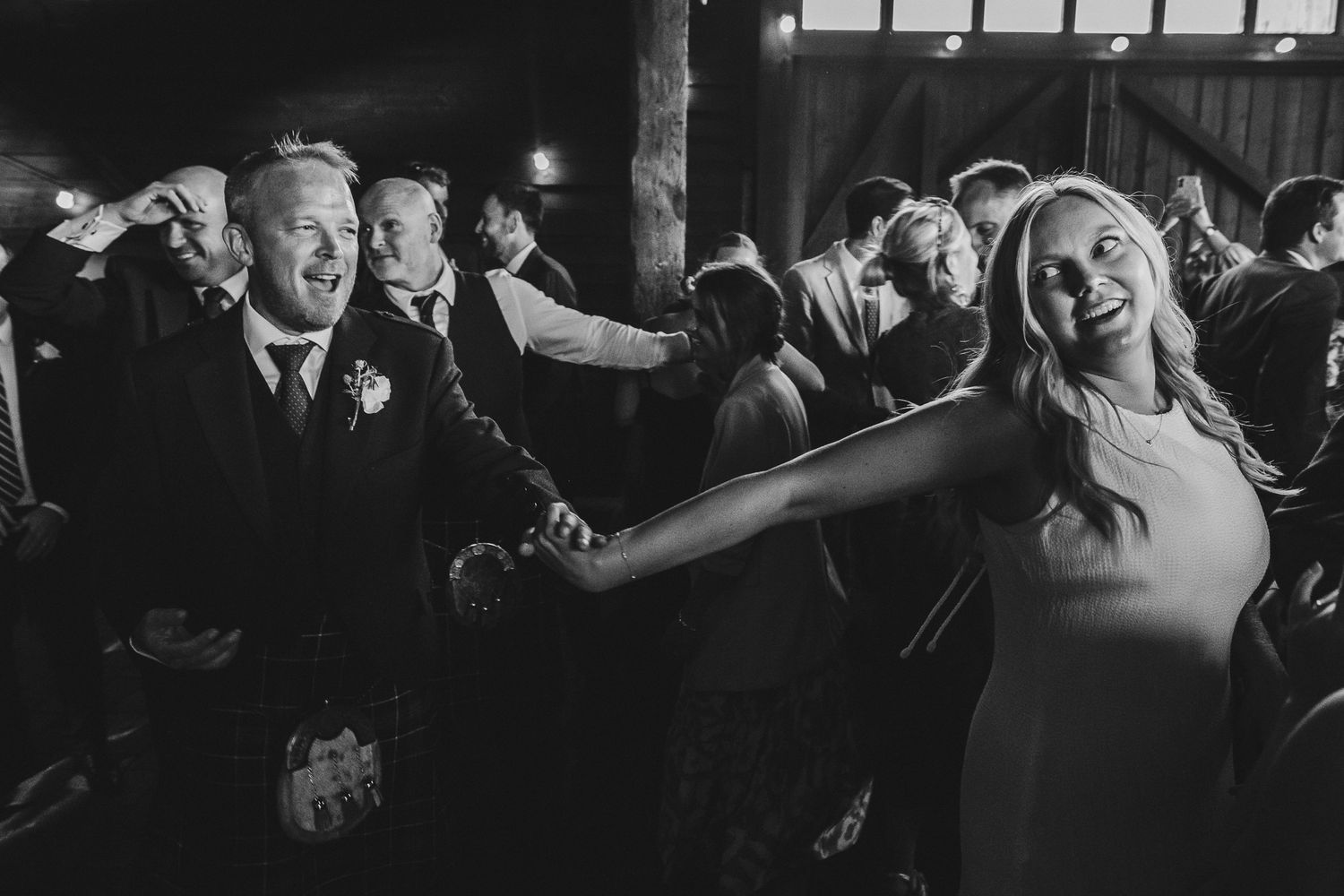 Wedding guests dance and celebrate joyfully on a crowded dance floor during an evening reception.