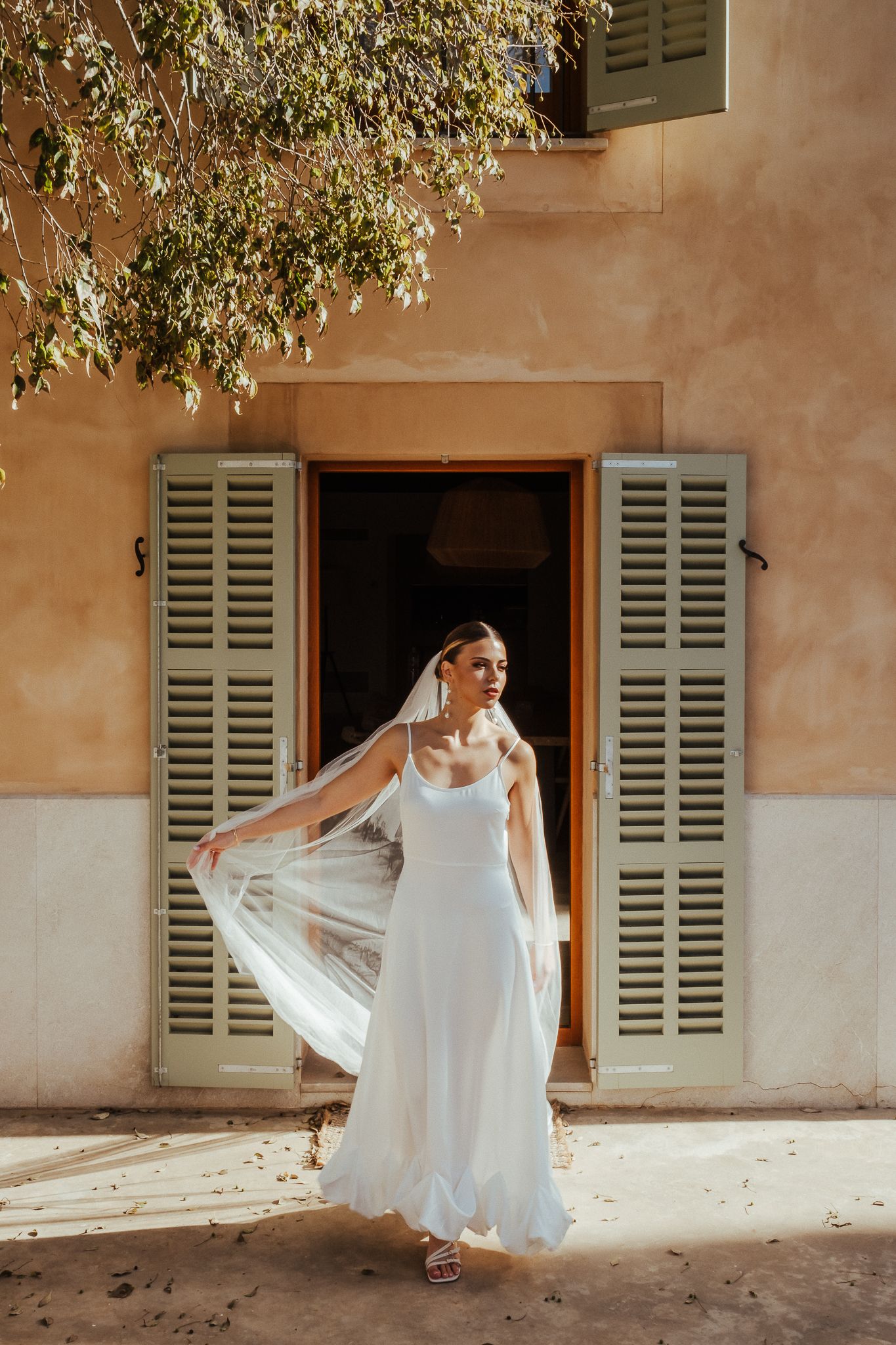 A sequence of five photos showing a flowing white dress in motion against a rustic Mediterranean building exterior.
