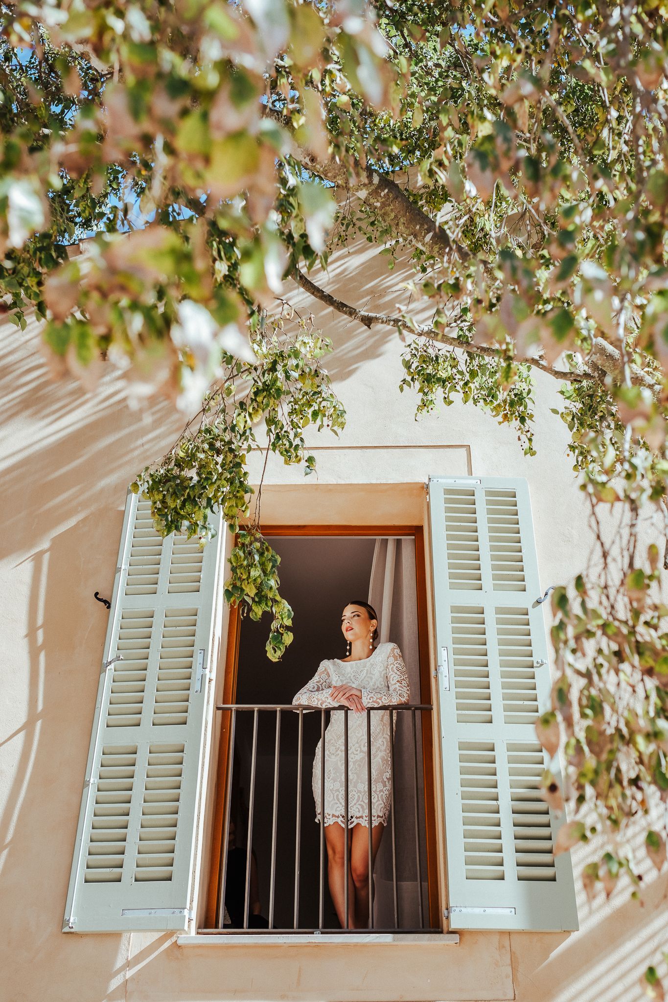 White shuttered window with tree branches framing the architectural detail of a Mediterranean style building.