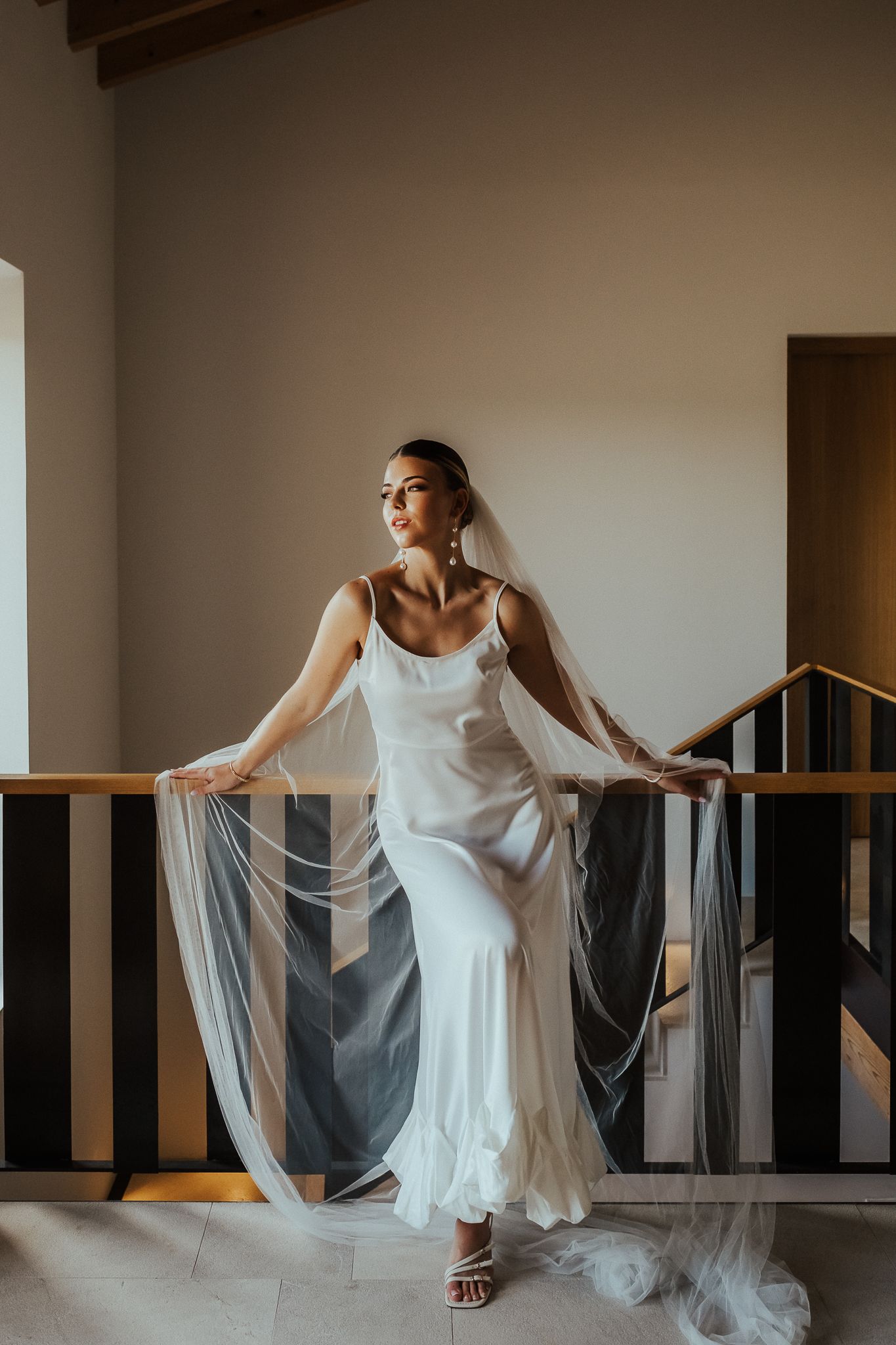 A graceful figure in a flowing white dress and veil creates an elegant bridal portrait sequence against neutral walls.