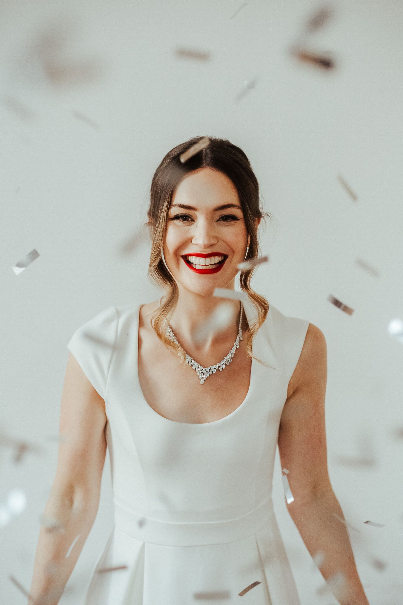 A series of four photos showing someone in a white wedding dress smiling with red lipstick and sparkling jewelry.