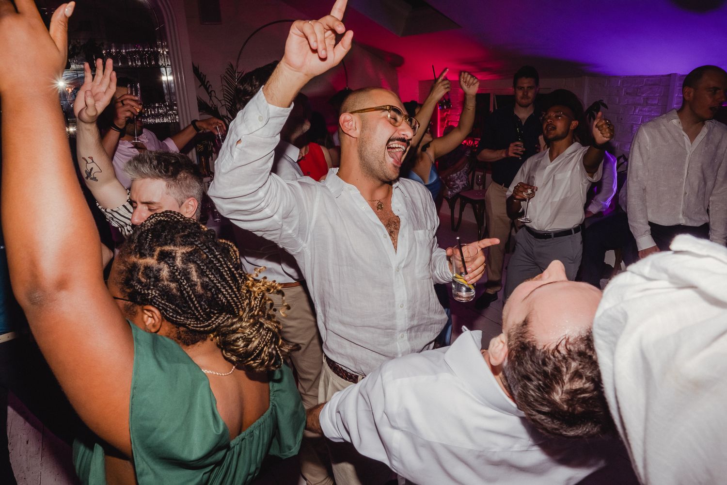 People dancing and celebrating at a lively party with purple and pink lighting in the background.
