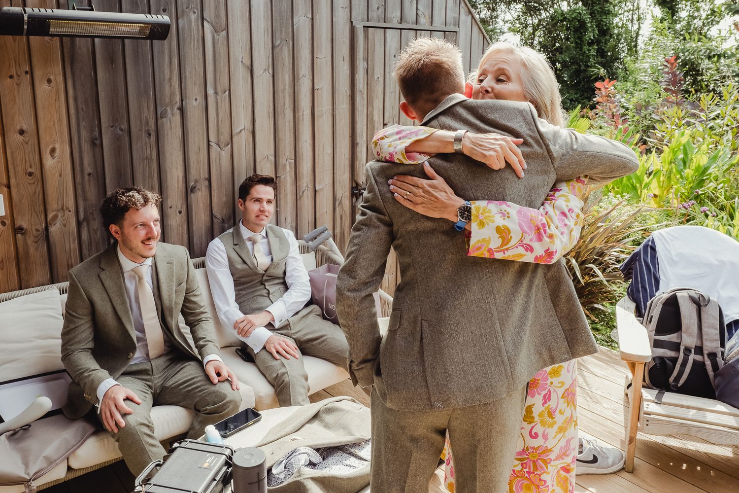 A couple sits together on a rustic wooden bench during an outdoor garden wedding celebration.