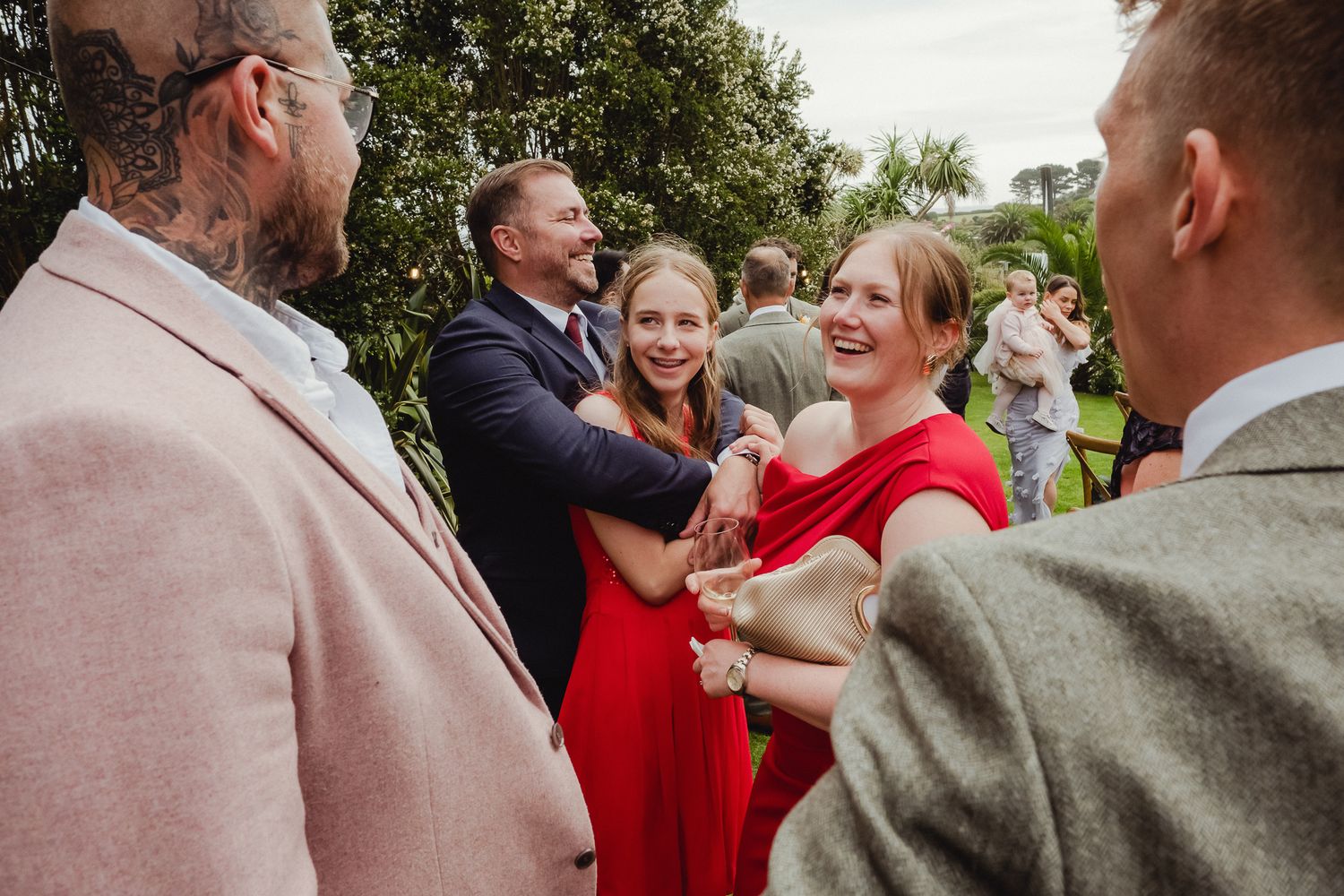 Wedding guests embrace and celebrate during an outdoor reception in a garden setting.