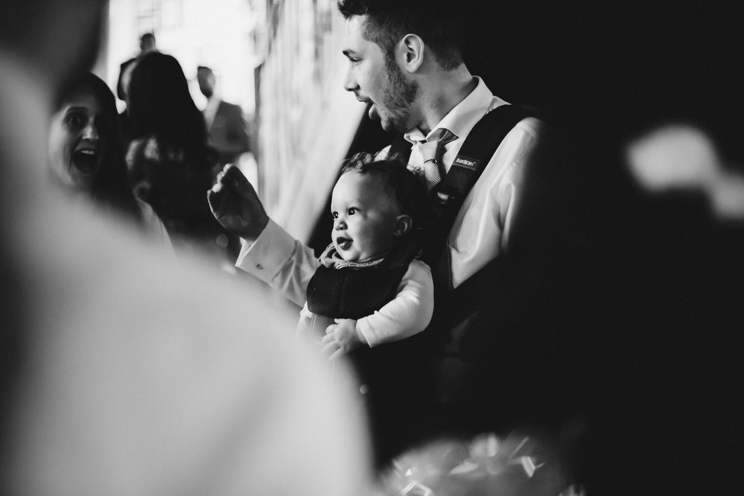 Black and white candid moment of guests laughing during wedding celebration.