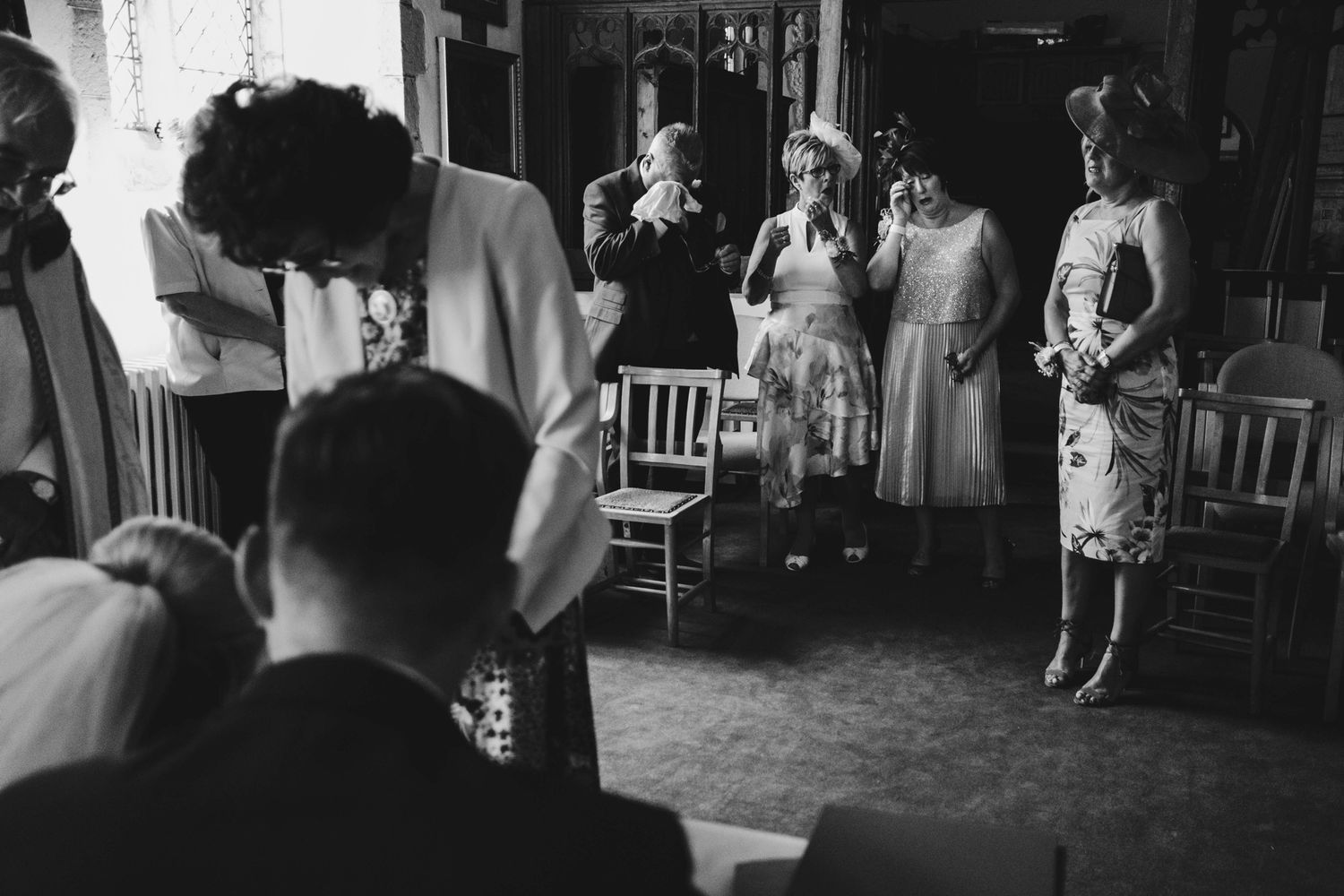A candid black and white photo of wedding guests interacting during a reception.
