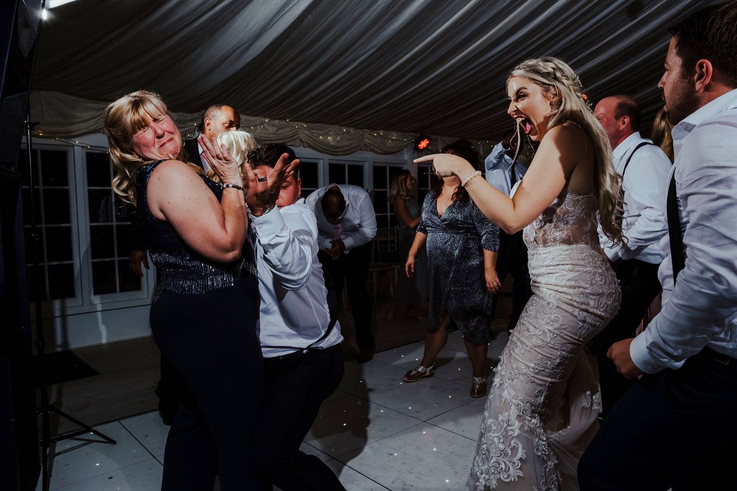 Wedding guests dance enthusiastically at a reception party in a covered venue.