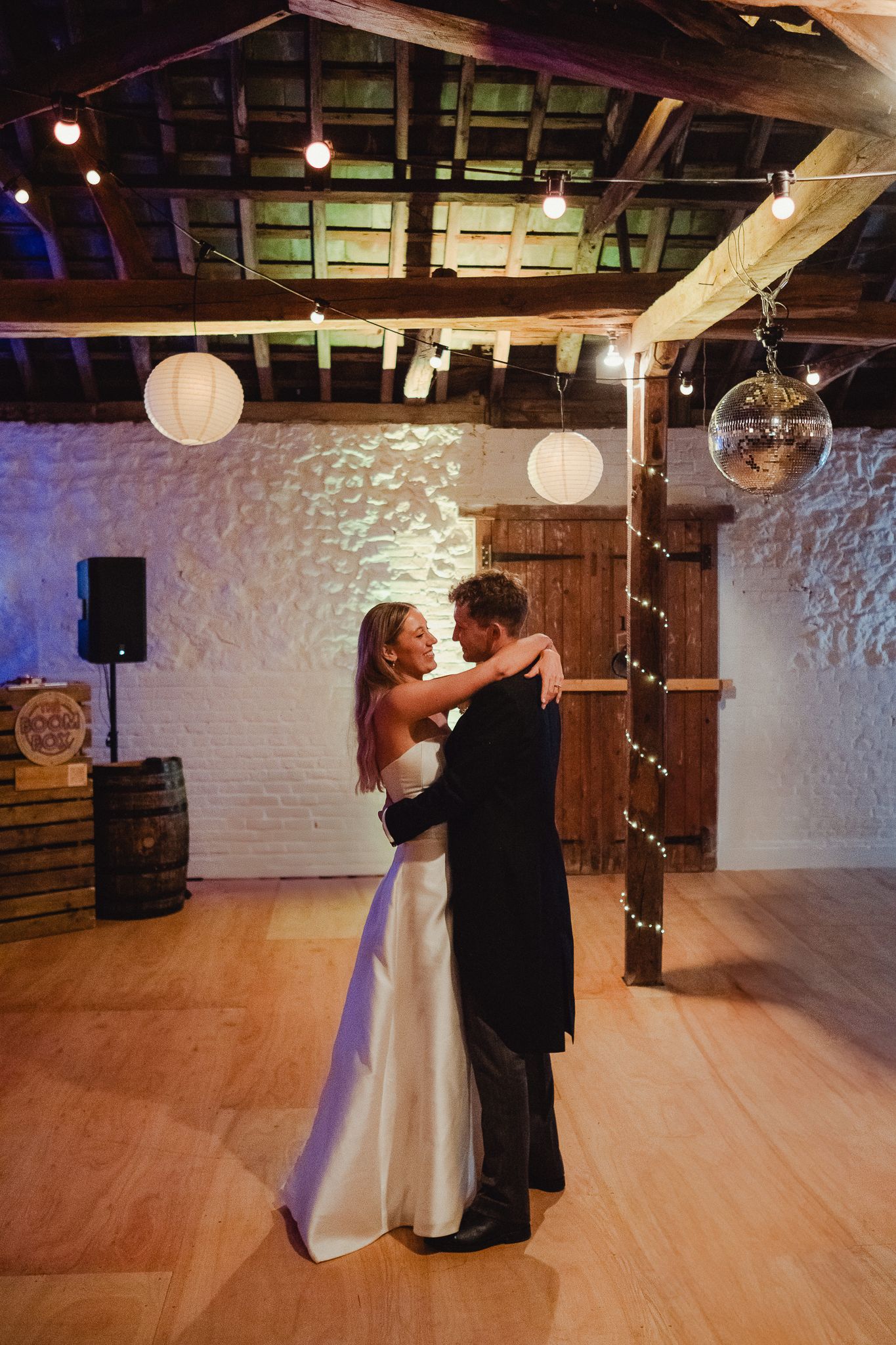 A romantic dance sequence on a polished wooden floor in a rustic venue with white walls and hanging lanterns.