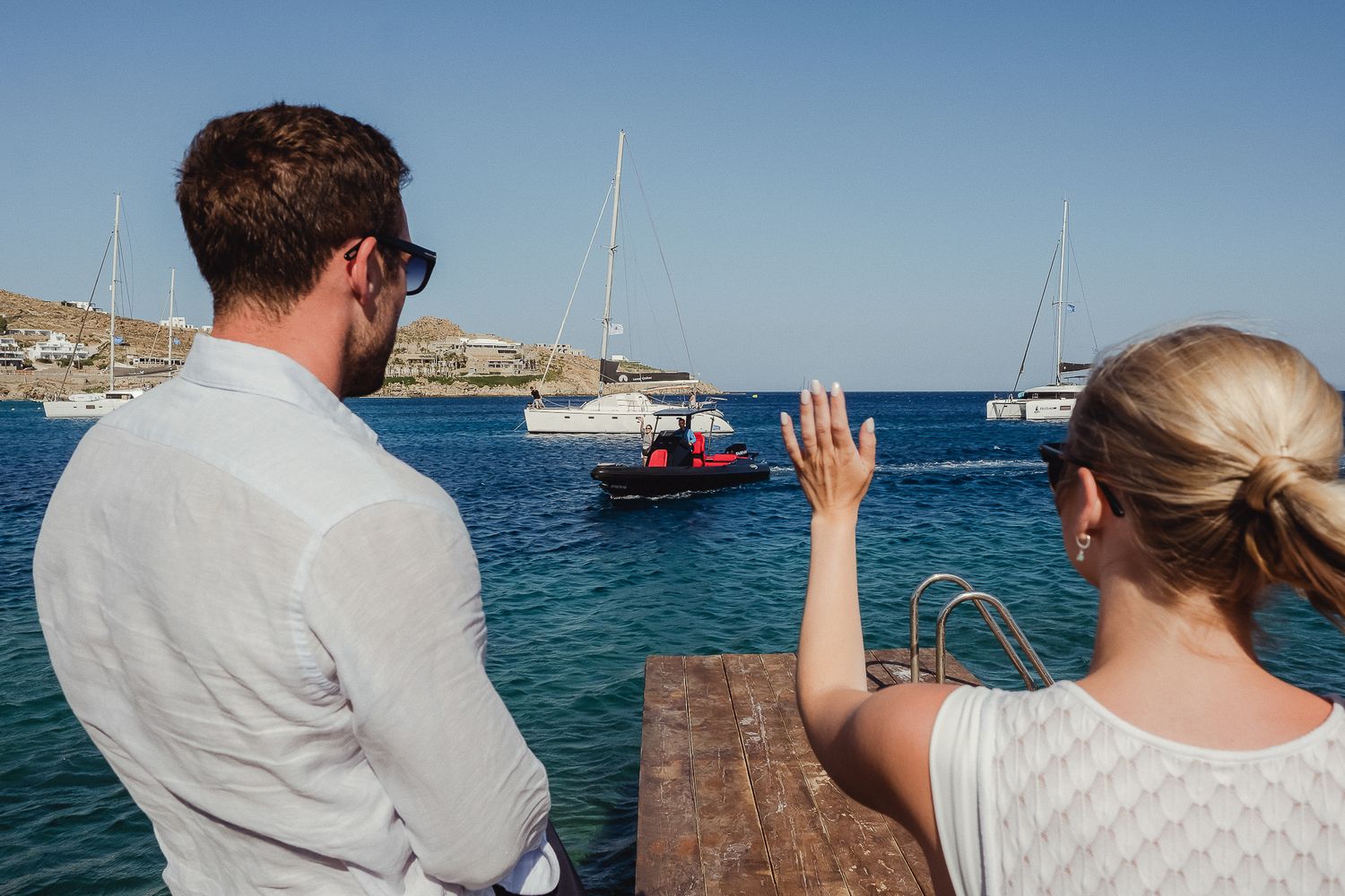 People enjoying a scenic boat tour along beautiful blue waters with multiple yachts and vessels visible in the harbor.
