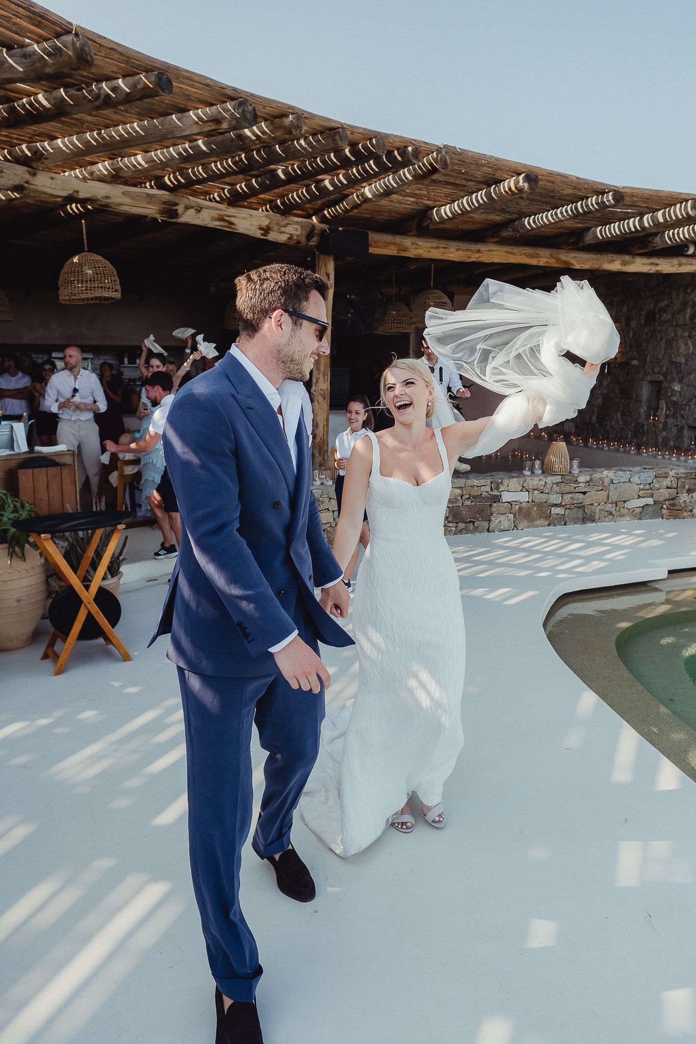 A couple dances together at an outdoor wedding venue with a thatched roof pergola and poolside setting.