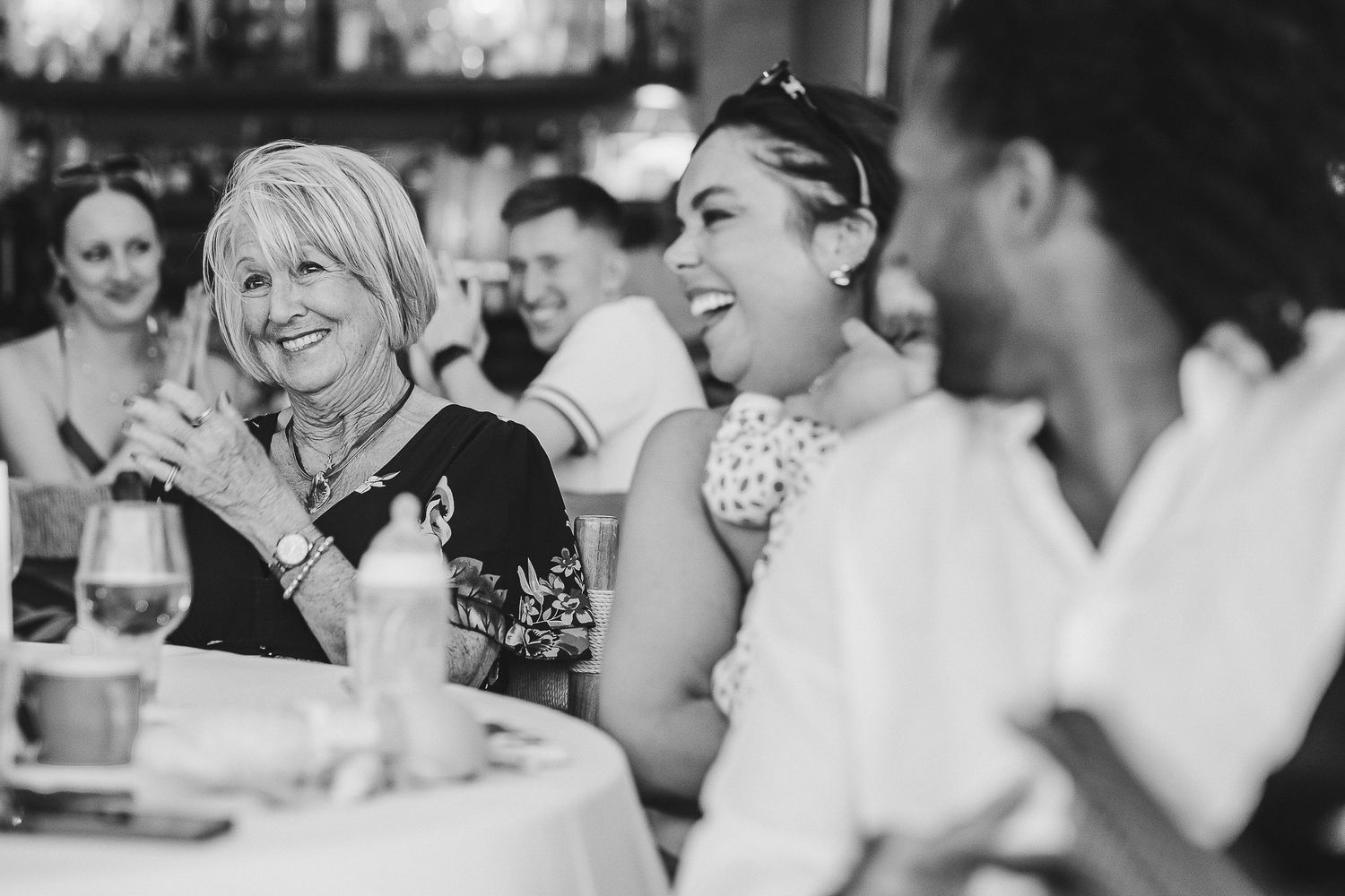 Black and white photo collage showing candid moments of laughter and joy during a wedding reception celebration.