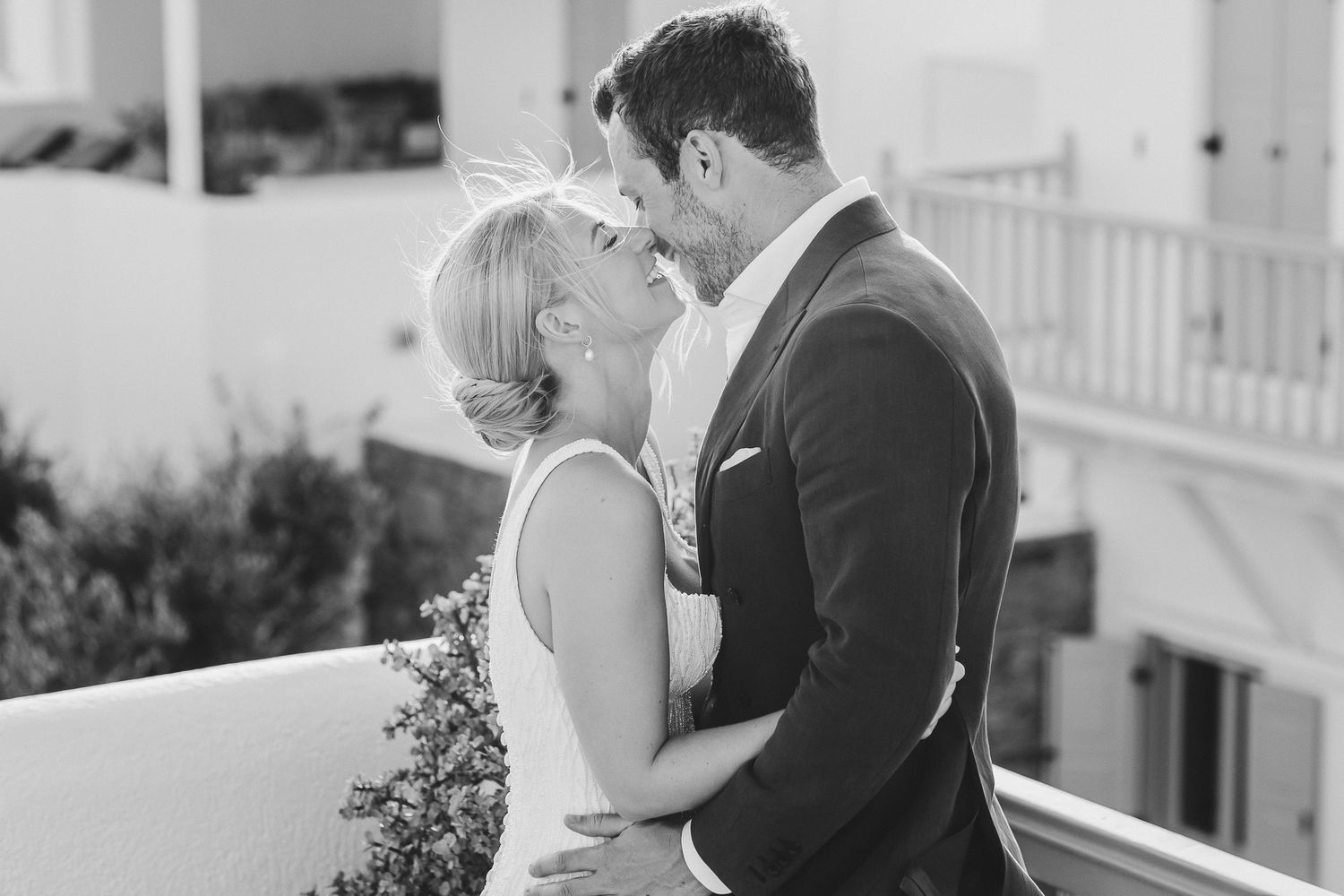 A couple shares an intimate moment on a white balcony in black and white photography.