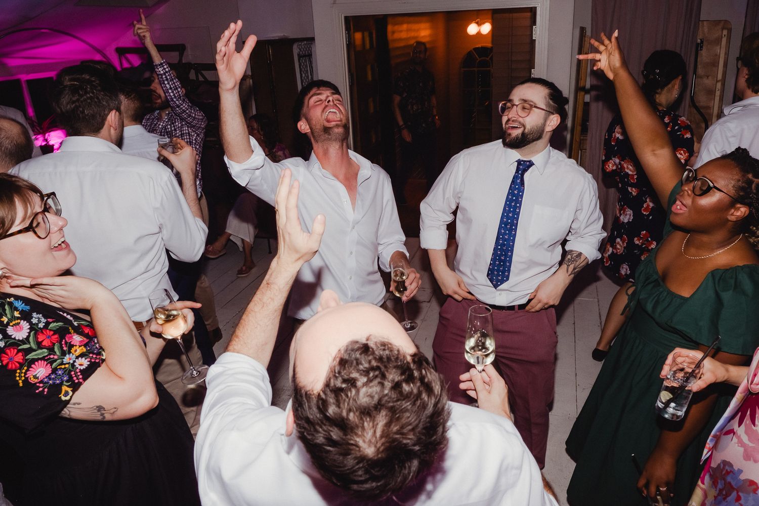 Wedding guests dance and celebrate on a dimly lit dance floor at an evening reception party.