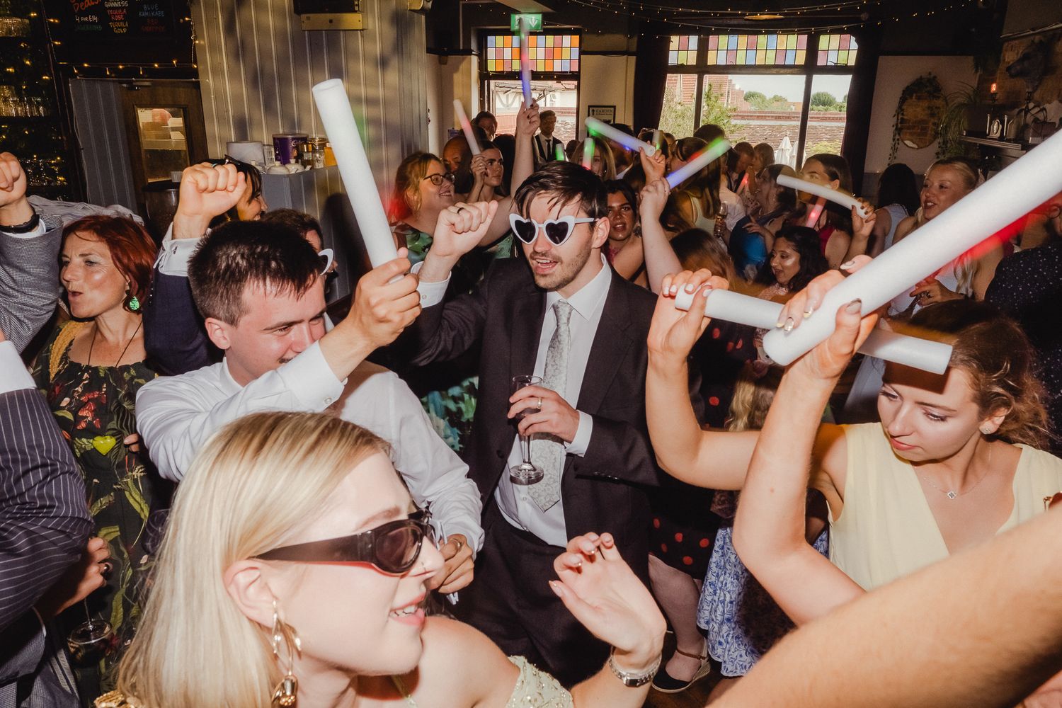 A lively wedding reception dance floor filled with guests celebrating and dancing with their hands in the air.