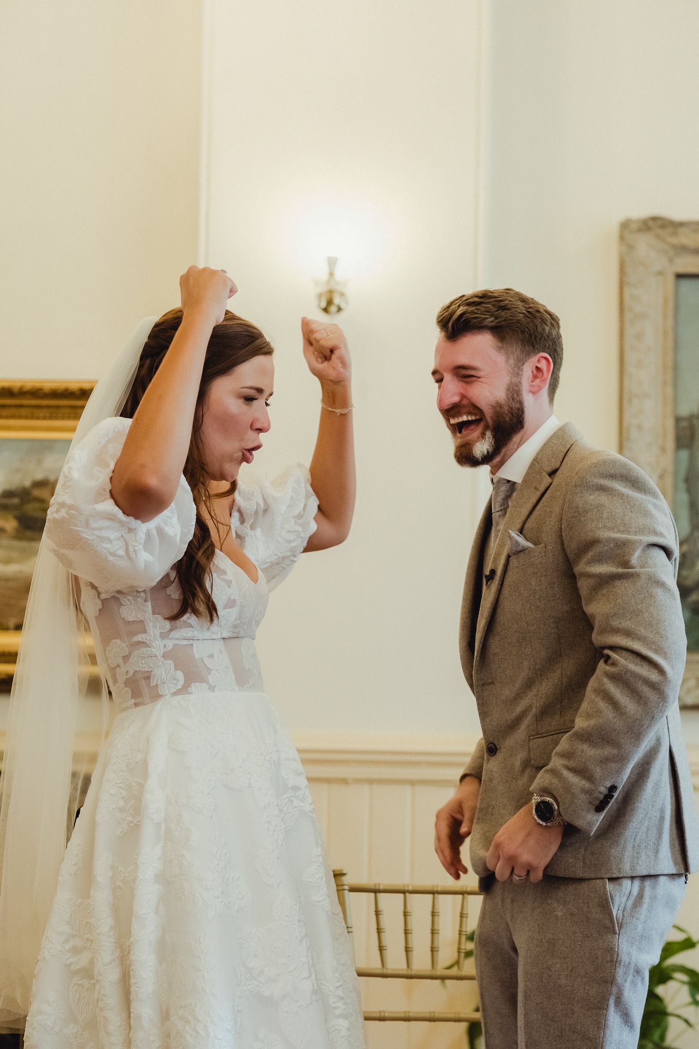 A couple shares joyful laughter during their first dance at a wedding reception in a bright indoor venue.