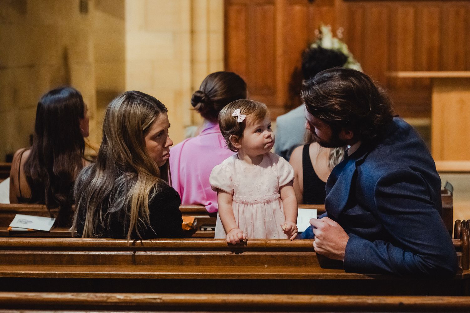 Students sitting together in wooden pews while looking at their mobile phones during a gathering.