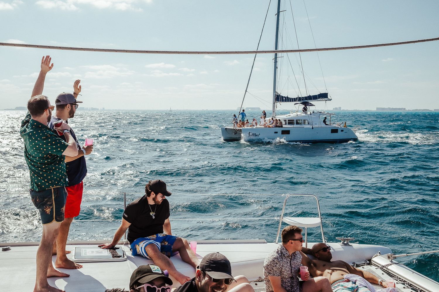 People enjoying a sunny day of sailing on a boat in blue ocean waters with other vessels visible in the distance.