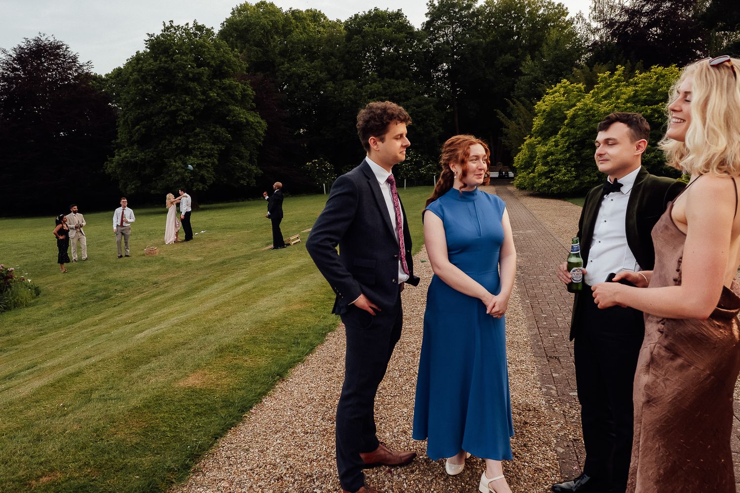 Elegantly dressed guests socializing on a gravel path at an outdoor garden wedding reception.