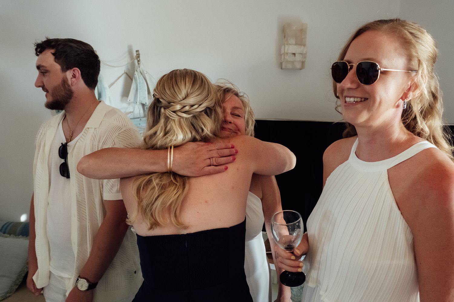 Two blonde women hugging at a celebration while friends smile nearby, one holding a wine glass.