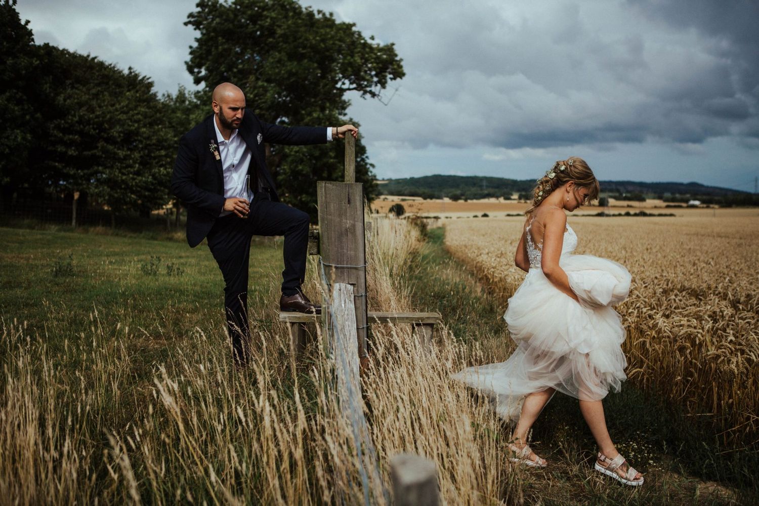 Playful wedding photo in a wheat field with stormy skies.