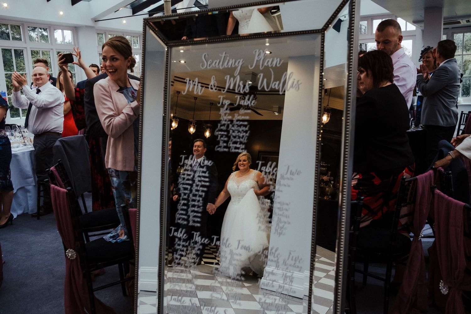 Wedding seating chart displayed on mirror at reception venue.