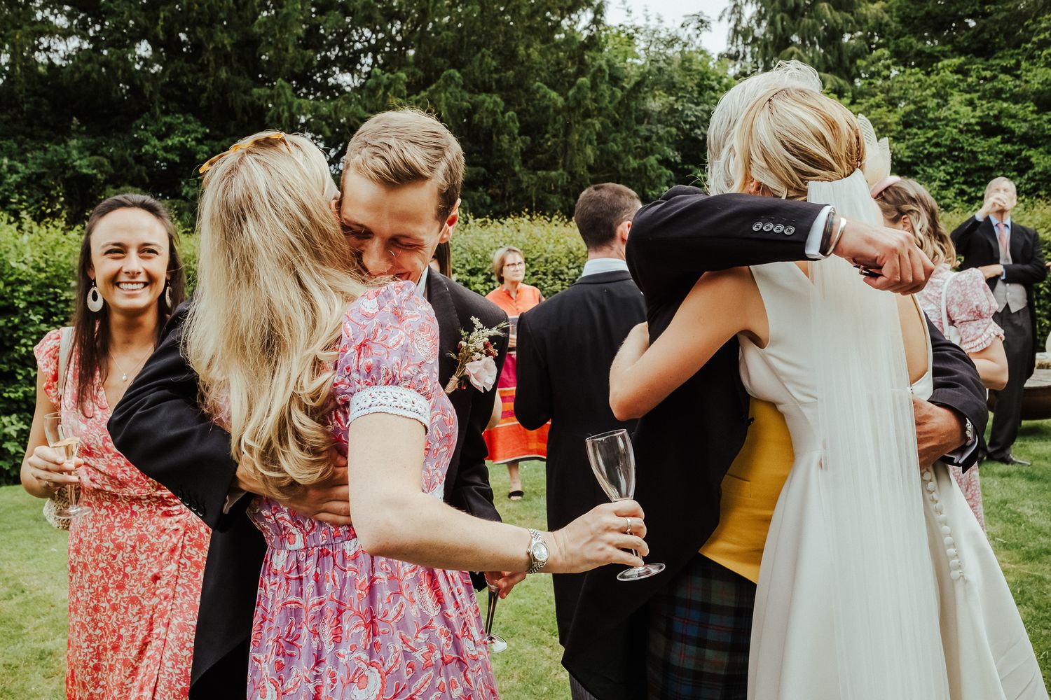 Wedding party enjoying candid moments at an outdoor garden reception with natural lighting.