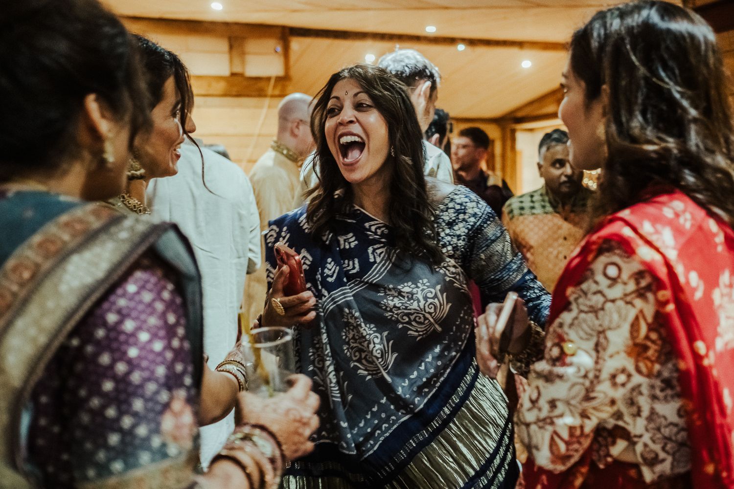 Party guests in traditional dress dance and celebrate at an indoor reception.