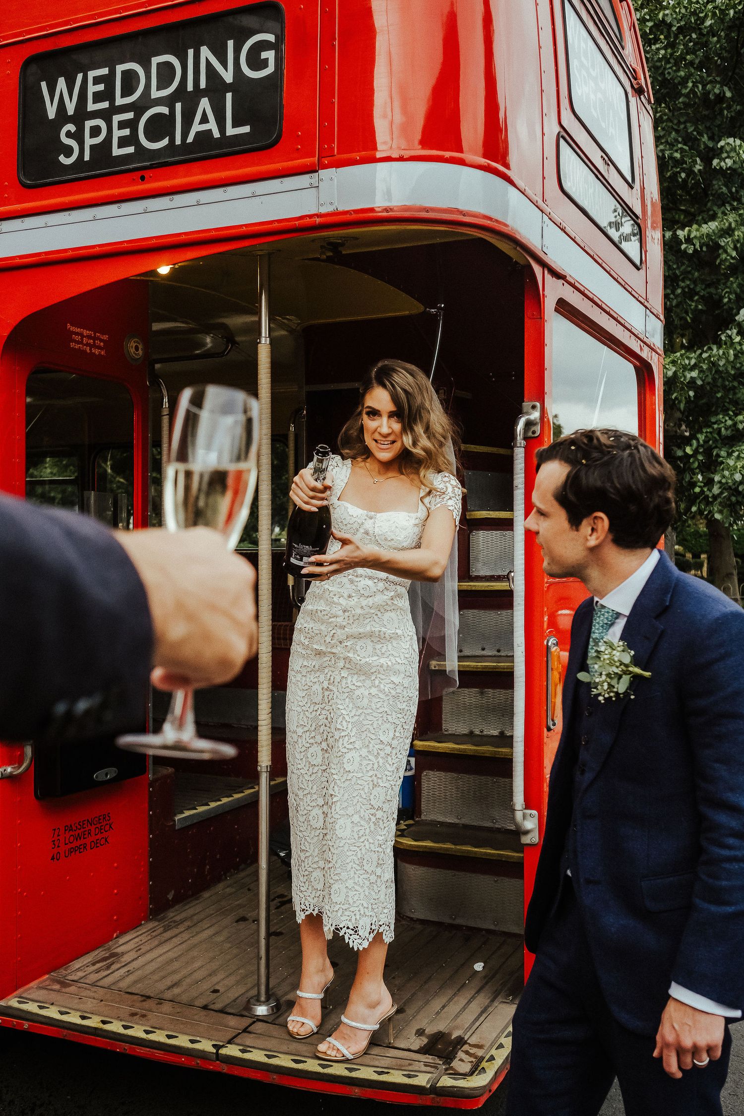 A couple shares a joyful moment boarding a classic red London double-decker bus decorated for a wedding celebration.