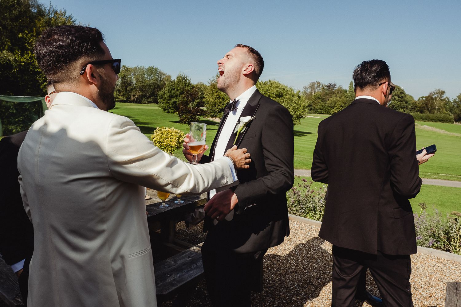 Candid moment of guests laughing together at an outdoor wedding celebration on a sunny golf course.