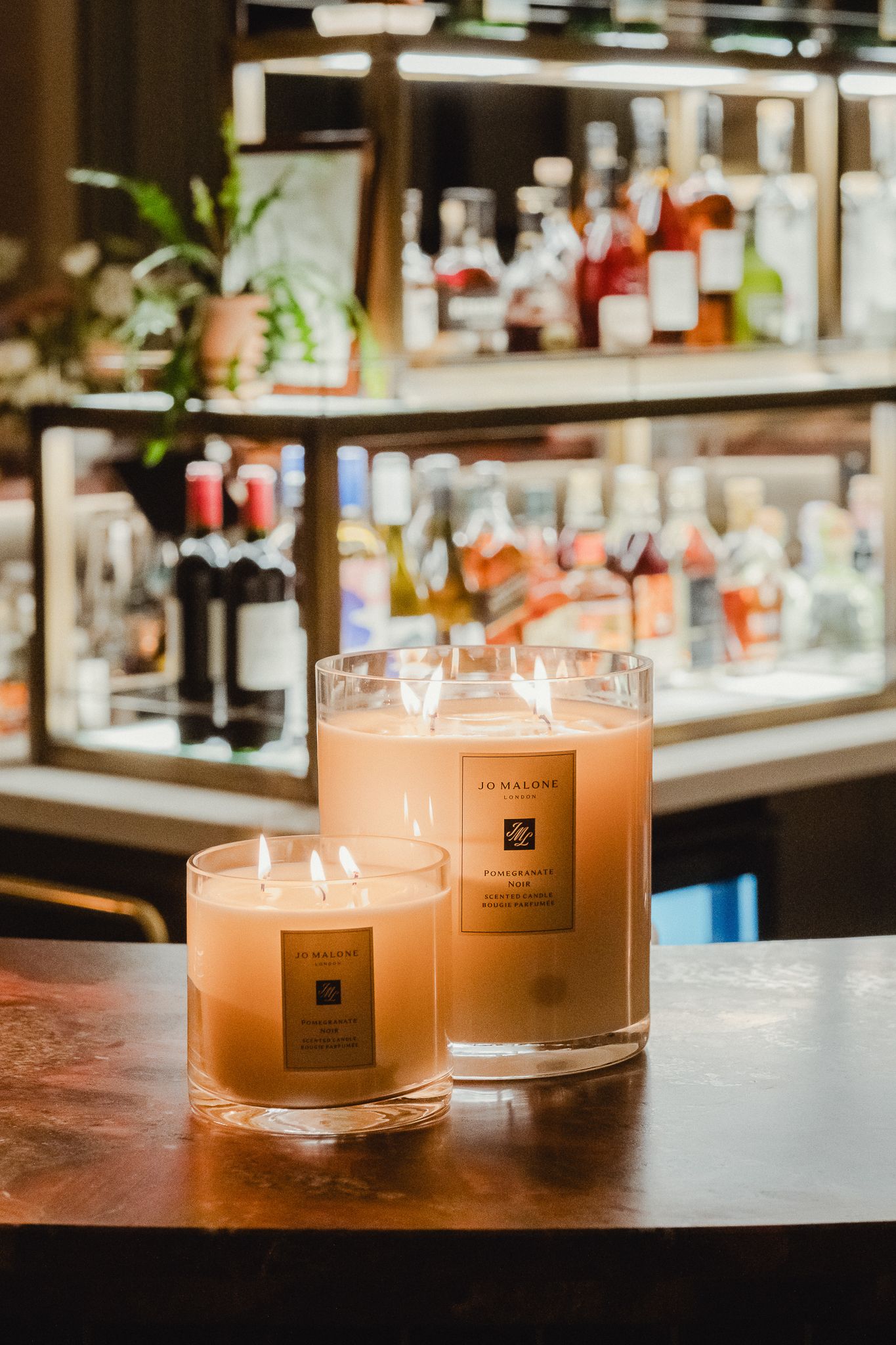 Glowing scented candles in glass jars arranged on a wooden bar counter.