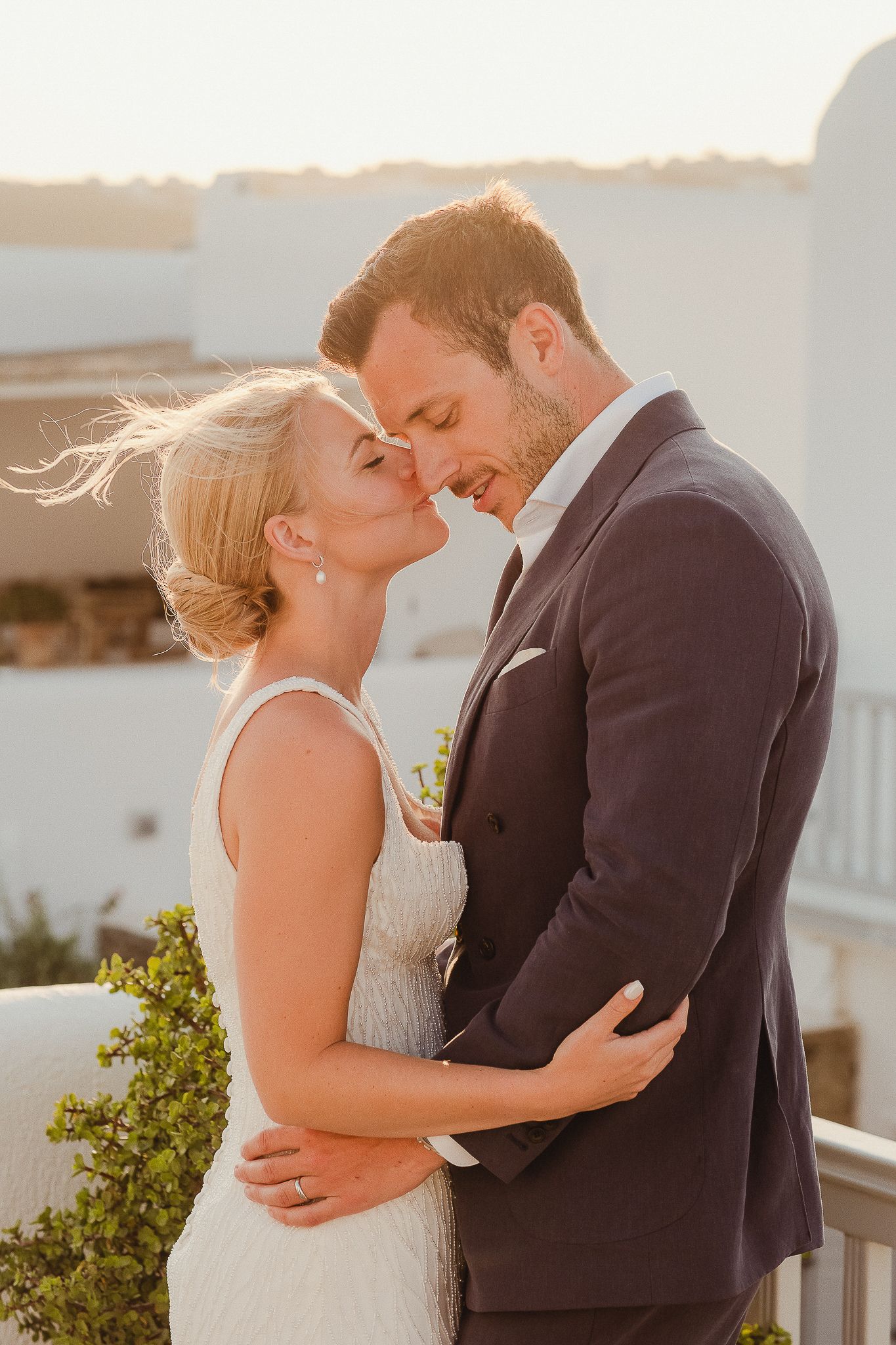 A romantic couple shares an intimate sunset kiss on a seaside balcony during their wedding celebration.