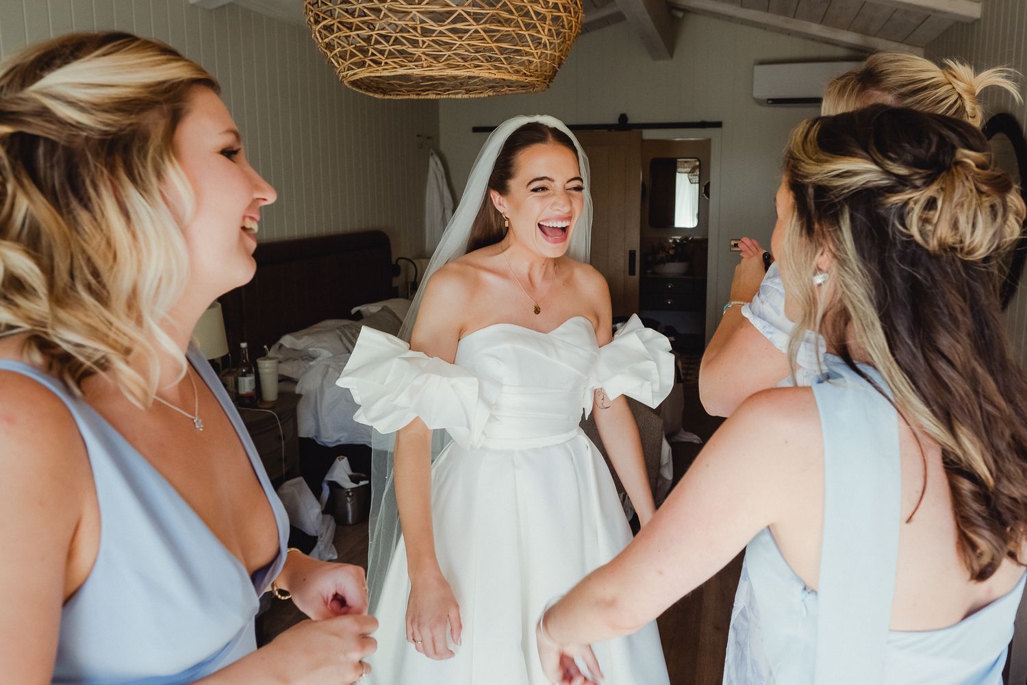 A group of bridesmaids in light blue dresses laugh and celebrate together during wedding preparations.