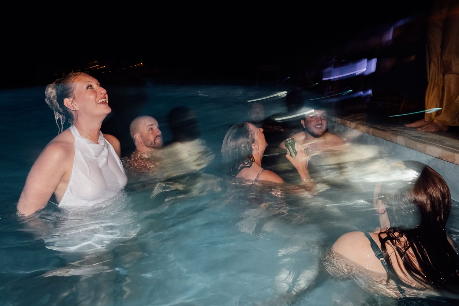 Group of people enjoying a hot tub together at night, laughing and socializing in warm water.
