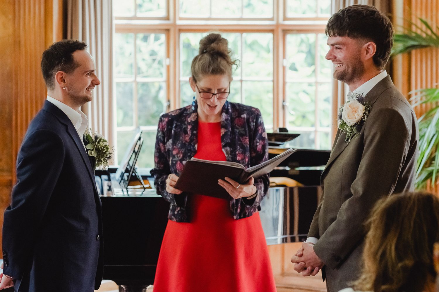 People gather for a ceremony in an elegant room with wood paneling and a grand piano in the background.