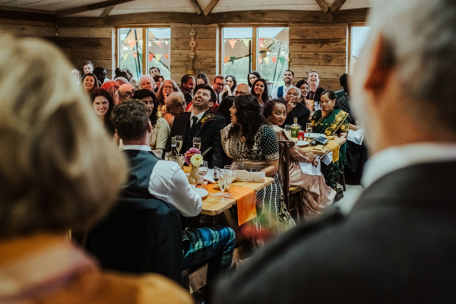 Wedding reception venue filled with guests celebrating at decorated wooden tables.