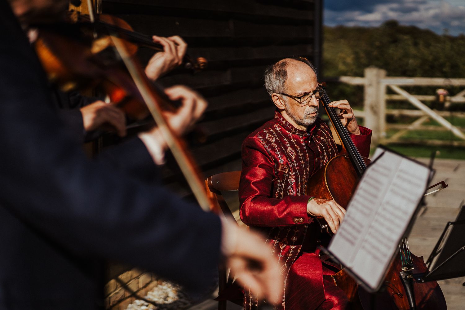 A musician in a red jacket performs while reading sheet music during an outdoor event.