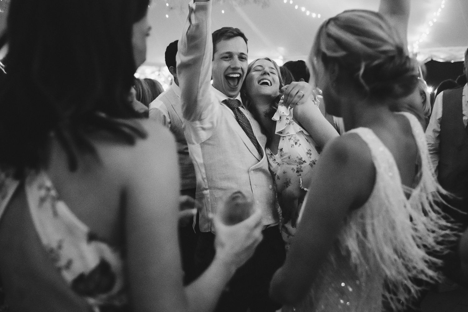 Black and white photo of wedding guests dancing and celebrating on a crowded dance floor.